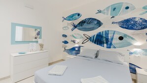 A modern bedroom with a bed, a dresser, a mirror, and a wall with fish artwork.