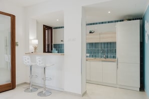 A modern kitchen with white cabinets, a blue backsplash, and two white bar stools.