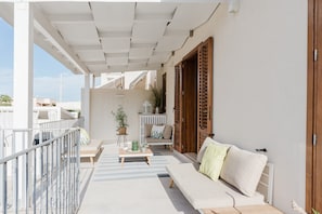 A balcony with a white pergola, a sofa, a small table with a plant, and a wooden door.