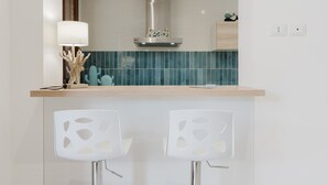 A kitchen with a stainless steel range hood, teal backsplash, wooden countertop, and two white chairs with cut-out patterns.
