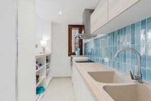A kitchen with two sinks, a window with blinds, and a shelf with kitchen items.