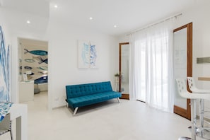 A modern living room with a blue sofa, a dining table, and a kitchen area in the background.