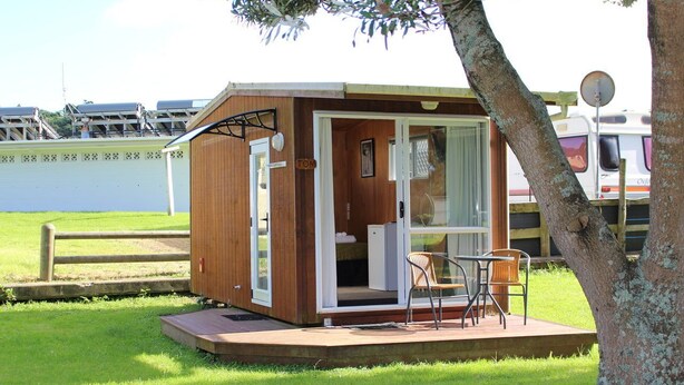 Une cabane en bois avec une porte en verre, une petite terrasse et deux chaises.
