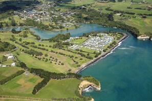 An aerial view of a coastal area with a marina, green fields, and a small residential community. - Urenui Beach Camp (Urenui)