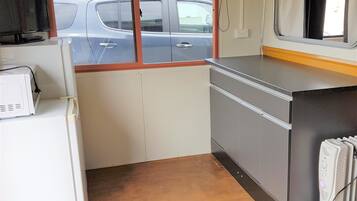 A compact kitchen with a refrigerator, microwave, and a small countertop. A window provides a view of parked cars outside.