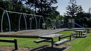 Une aire de jeux avec des balançoires et des toboggans, entourée d’arbres et de tables de pique-nique.
