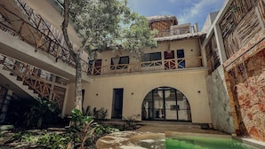 A courtyard with a pool, a tree, and a building with a thatched roof and wooden balconies. - "Lotus" Tulum Jungle Suite | Fast Wifi | Private Balcony (Tulum)