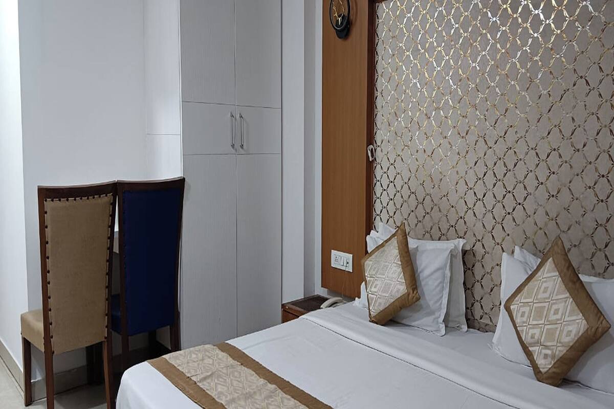 A hotel room with a bed, a wardrobe, a chair, and a patterned headboard.