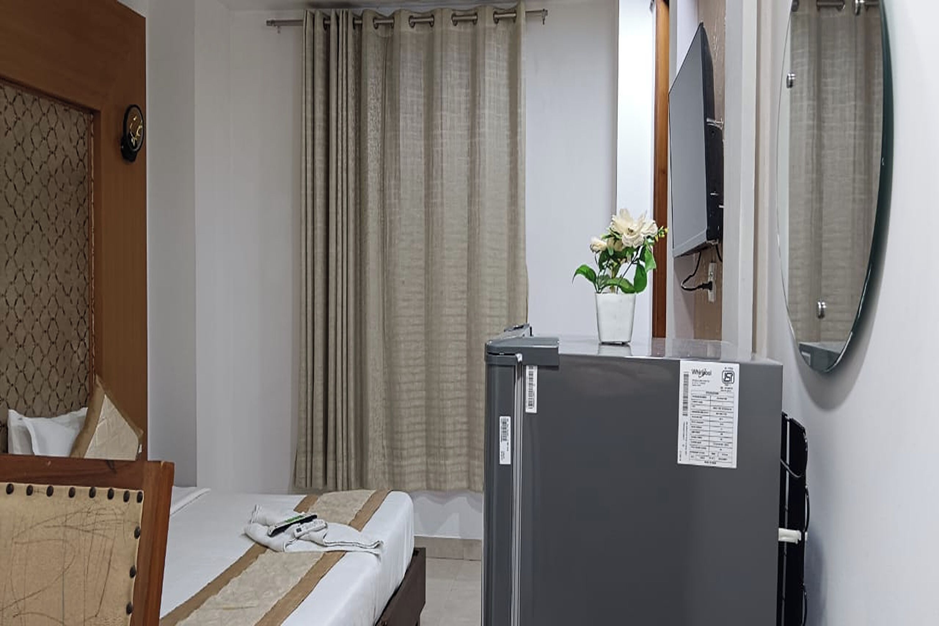 Habitación de hotel con cama, refrigerador, espejo y ventana con cortinas.