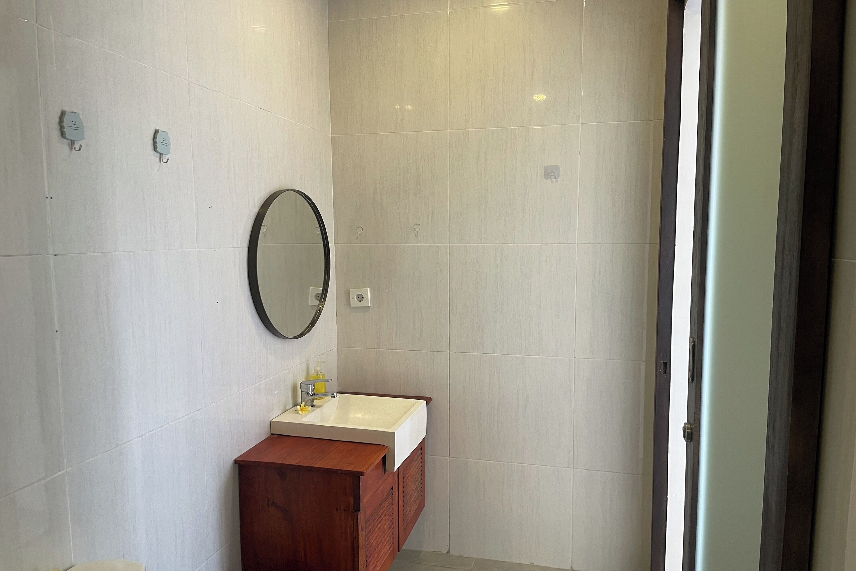 A bathroom with a white sink, wooden cabinet, and a round mirror on the wall.