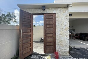 An open wooden door leading to a stone-walled area with a motorcycle parked outside. - Dayuh Villa (Kutuh)