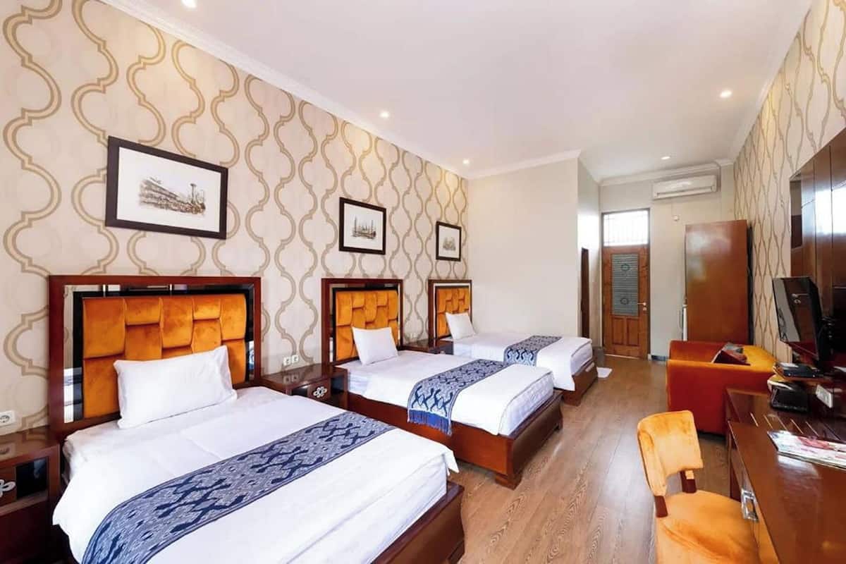 A hotel room with three beds, a desk, a chair, and a television.