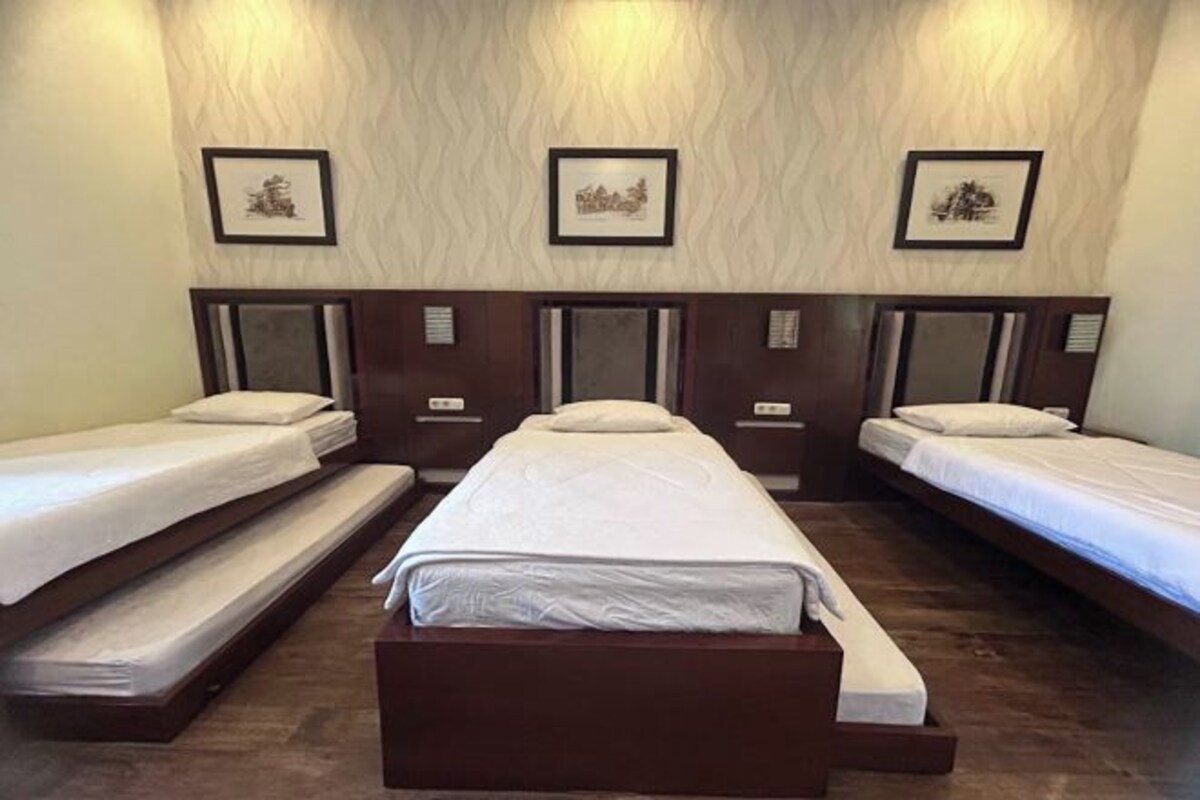 A hotel room with three single beds, each with a wooden headboard and white bedding. There are framed pictures on the wall above the beds.