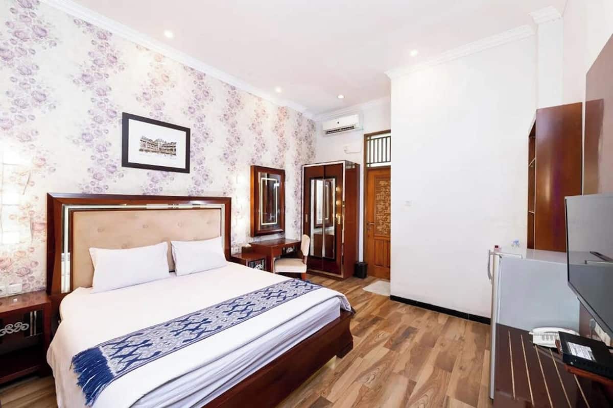 A hotel room with a large bed, wooden flooring, a TV, a desk, and a wardrobe.