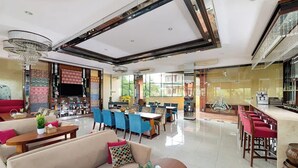 Un rebedor d'hotel espaiós amb un disseny modern, que inclou una zona de seients amb sofàs i cadires, una zona de dinar amb taules i cadires, i un penjador gran.