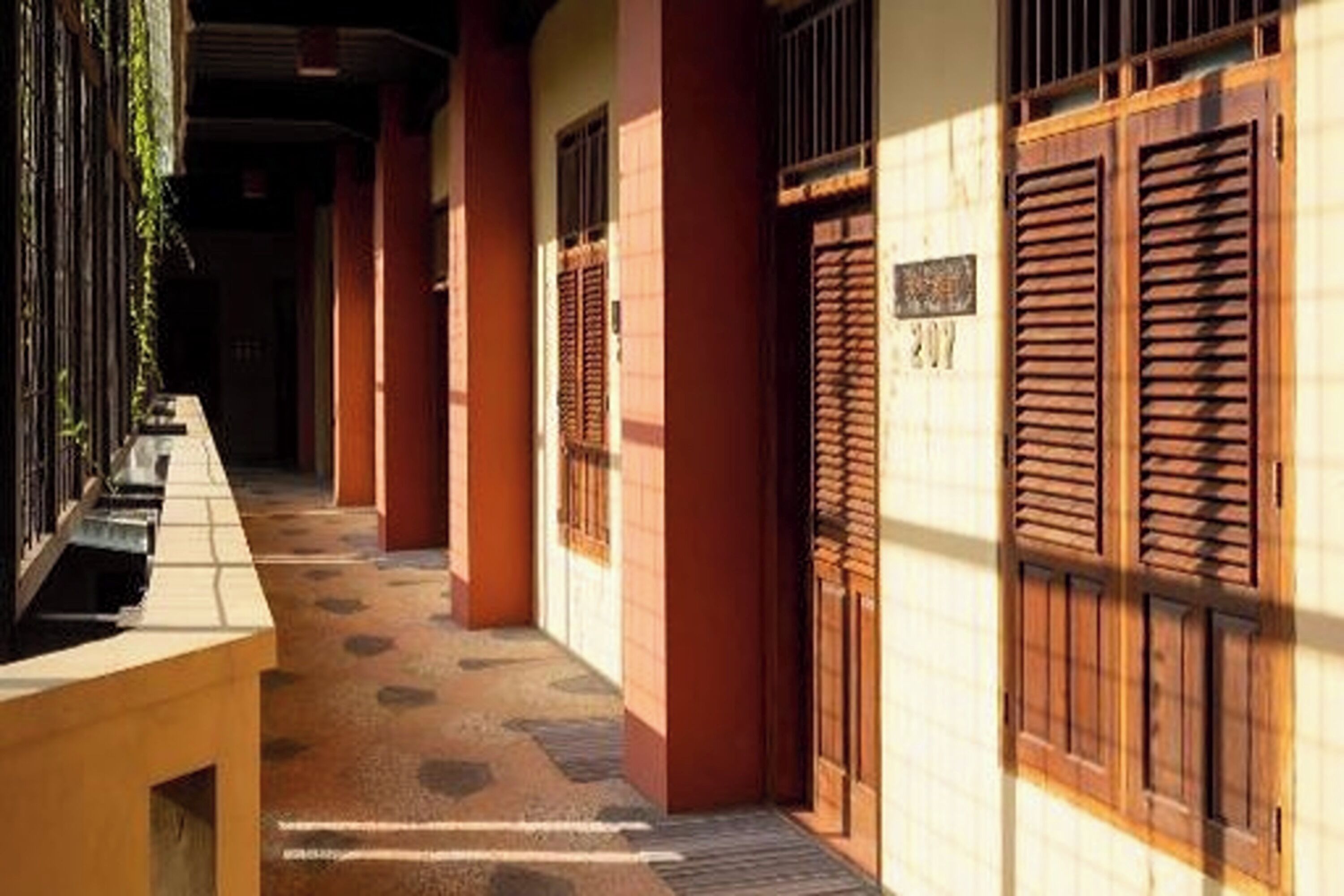A corridor with a bench, wooden shutters, and a tiled floor.