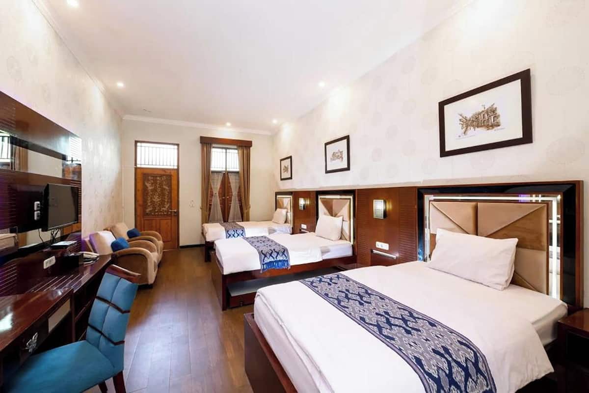 A hotel room with a large bed, two smaller beds, a desk with a chair, a TV, and a wooden door.