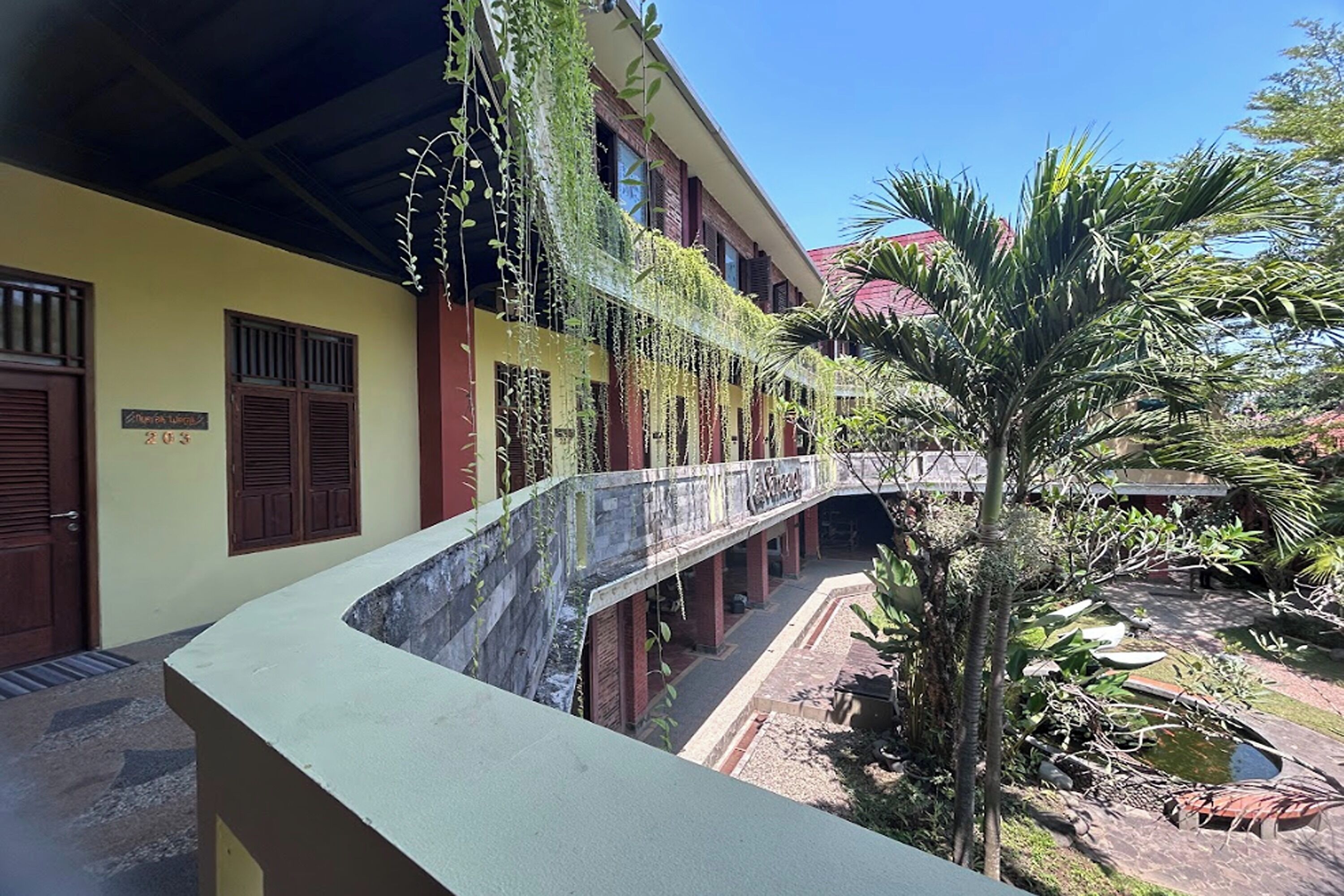 A building with a curved balcony, a small garden, and a palm tree.