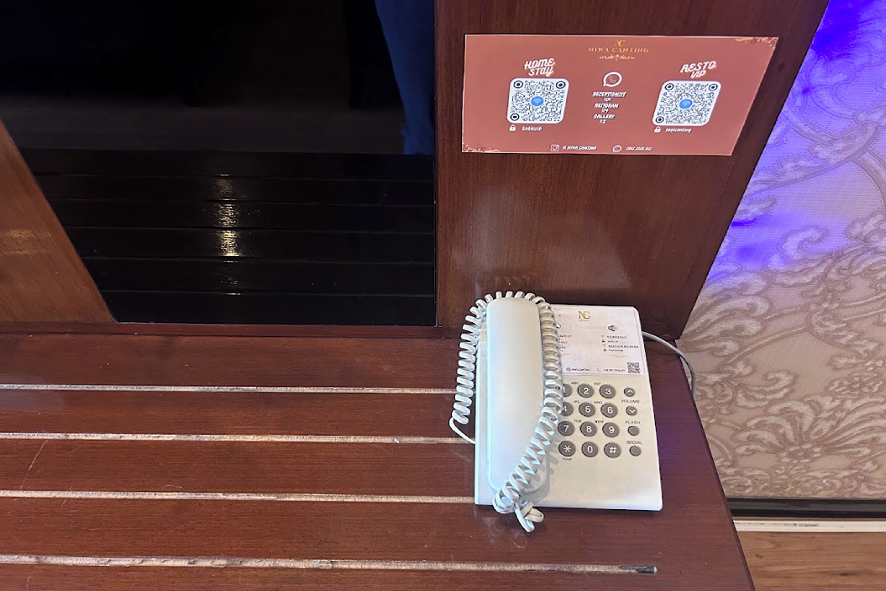 A wooden reception desk with a spiral-bound telephone and a QR code sign for 'home stay' and 'resto vip'.