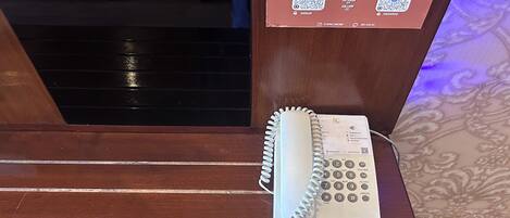 A wooden reception desk with a spiral-bound telephone and a QR code sign for 'home stay' and 'resto vip'.