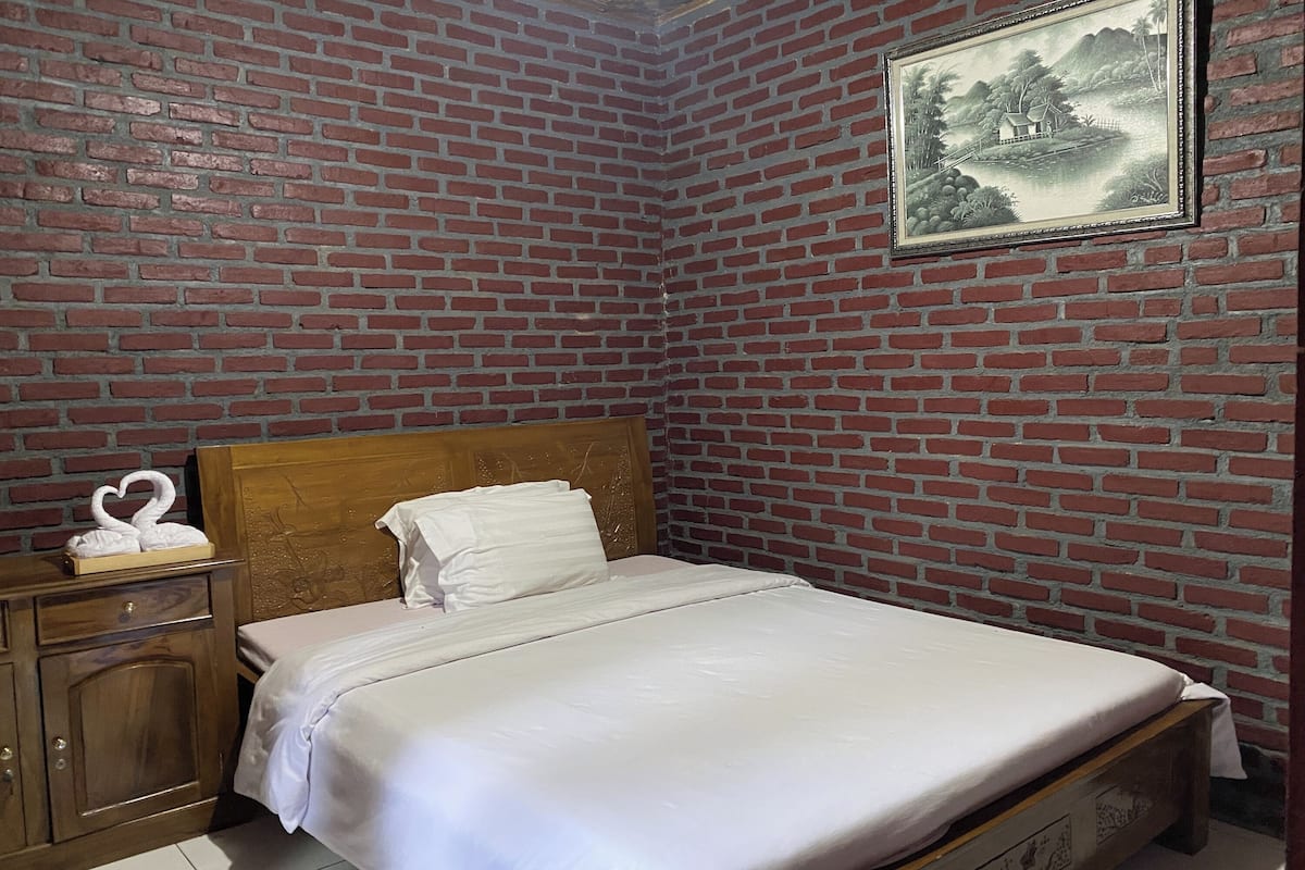 Cama bem arrumada em quarto com parede de tijolos e quadro emoldurado.