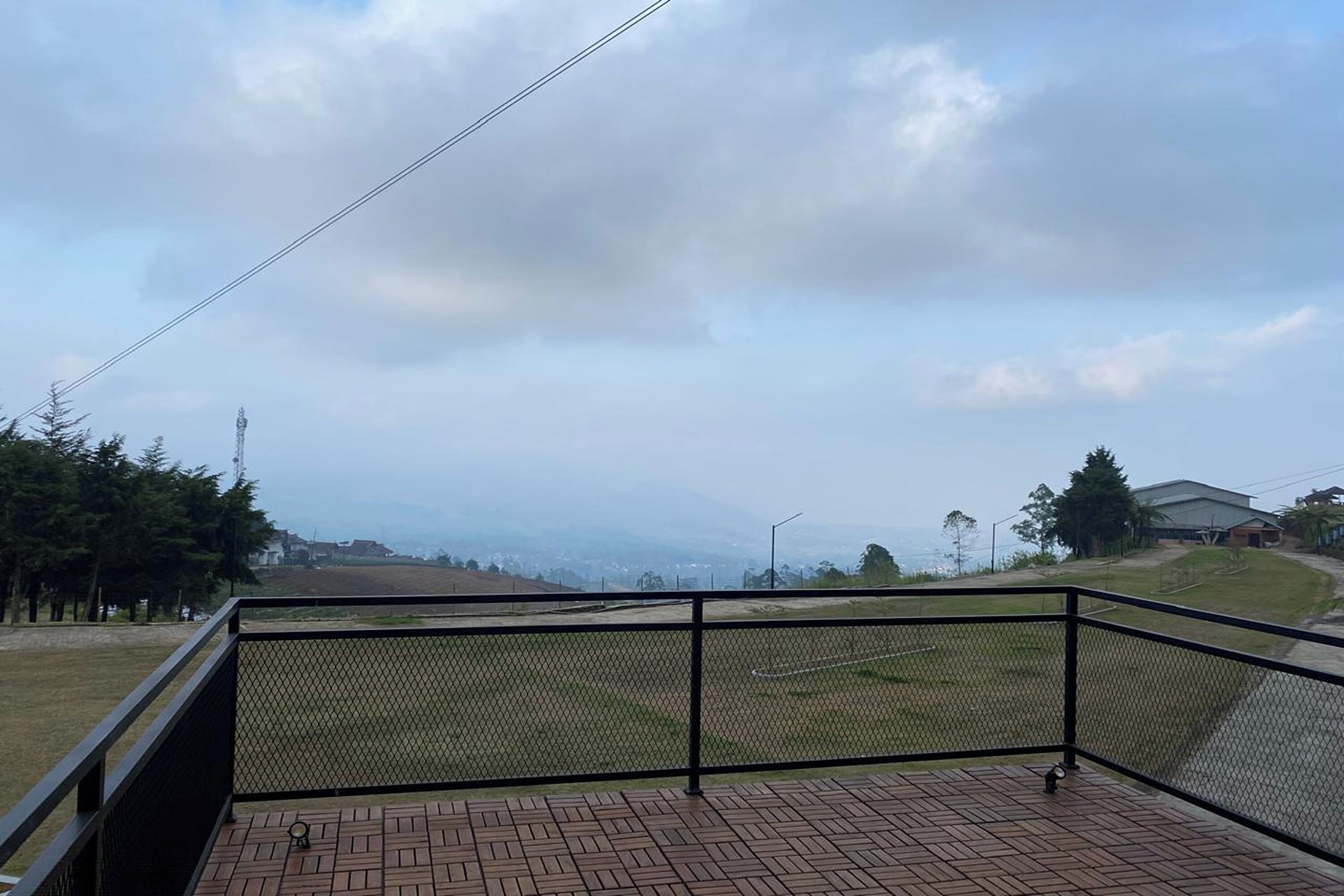 Un balcón con barandilla de metal que da a un área verde y edificios al fondo.