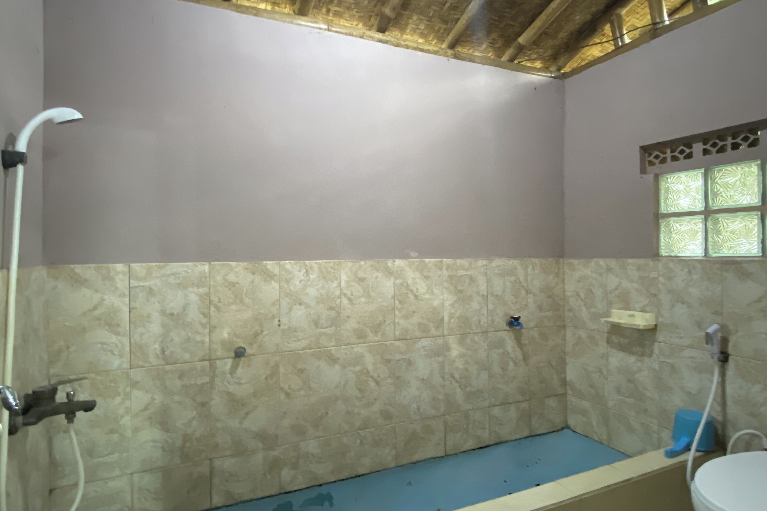 A bathroom with a shower, a toilet, and a window with decorative glass.