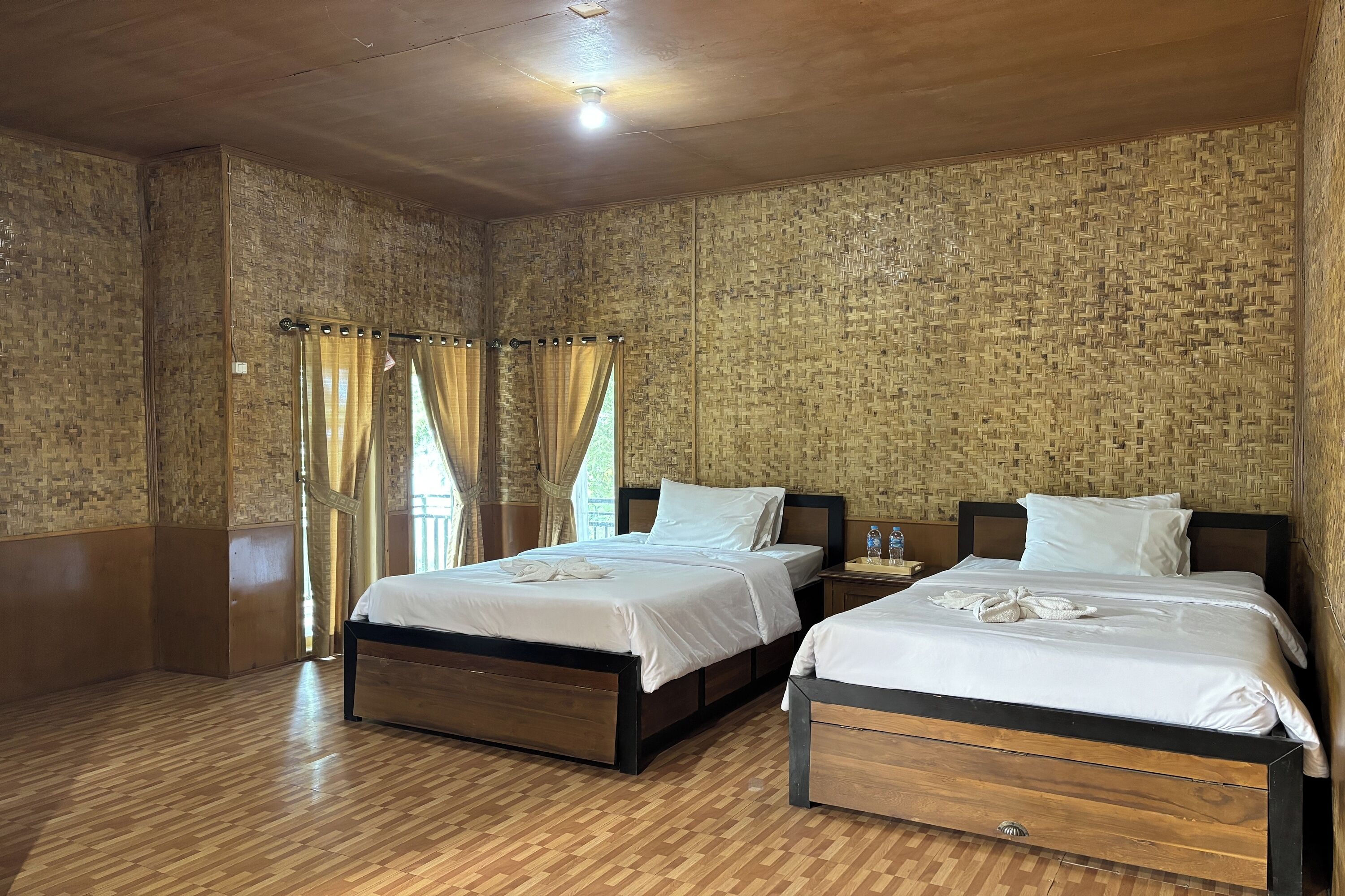 A room with two beds, wooden flooring, and a woven wall.