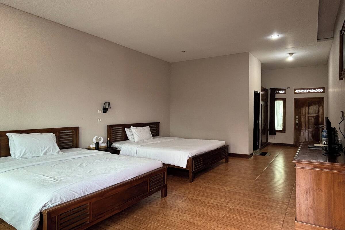 Quarto de hotel com duas camas de madeira, uma escrivaninha de madeira e uma pequena casa de banho.
