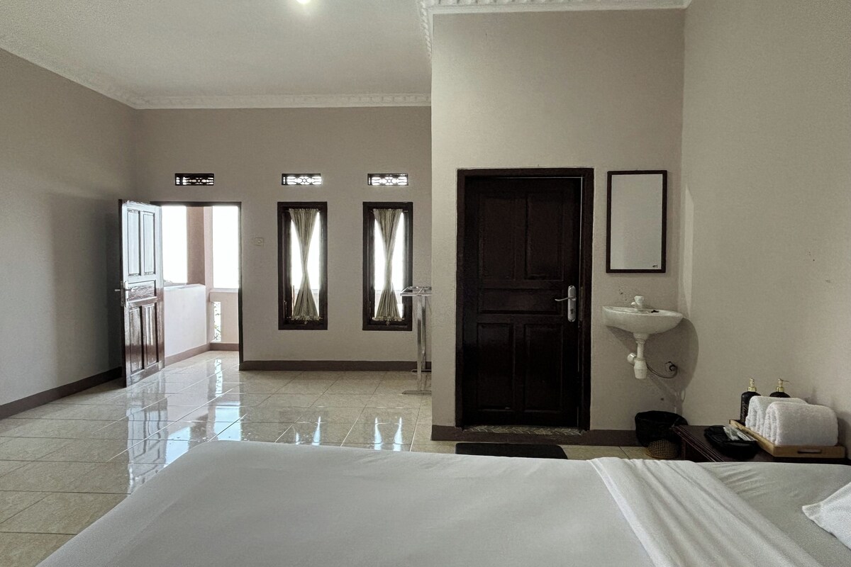 A hotel room with a large bed, a bathroom with a sink, and a view of the outside.