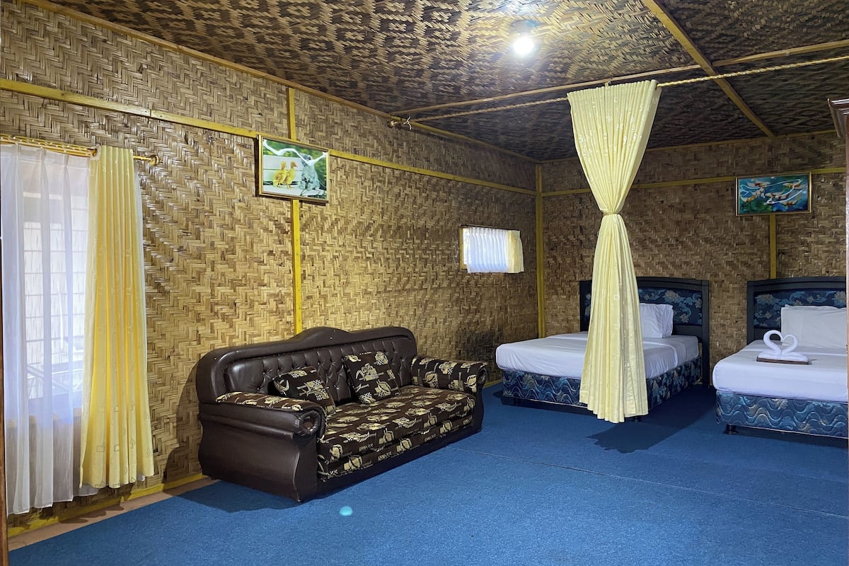Quarto com parede de padrão trançado, um sofá marrom, duas camas com roupa de cama azul e branca, e teto com design trançado.