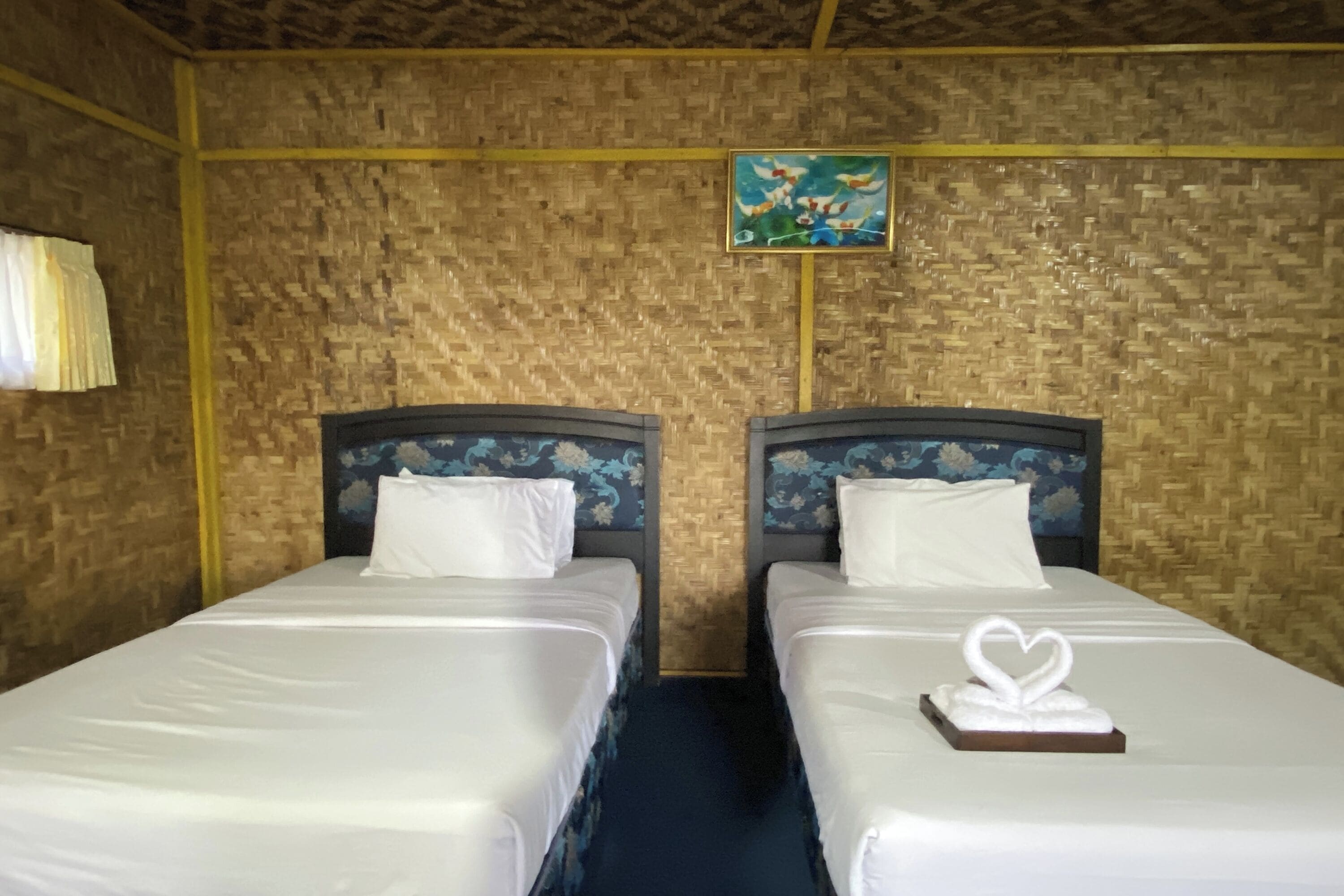 Una habitación con dos camas, cada una con cabecera y ropa de cama blanca. Hay un cuadro en la pared sobre las camas.