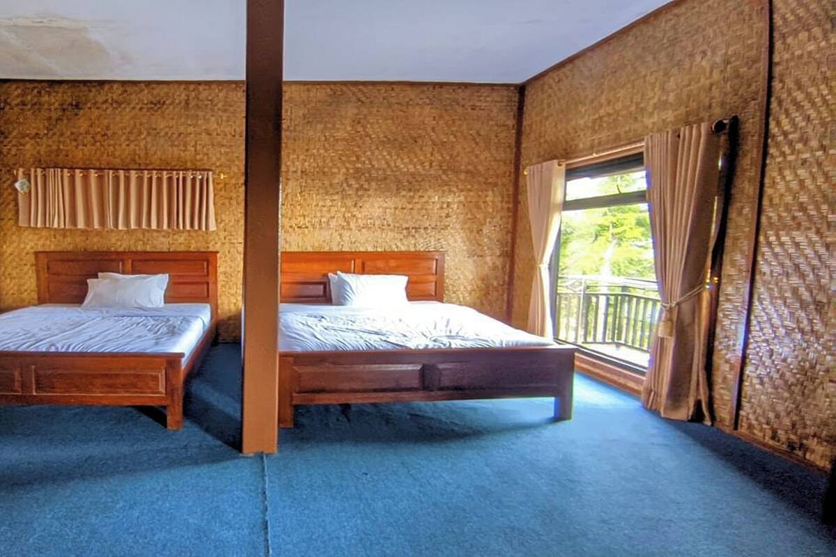 Um quarto com duas camas de madeira, uma janela com cortinas e vista para o verde lá fora.