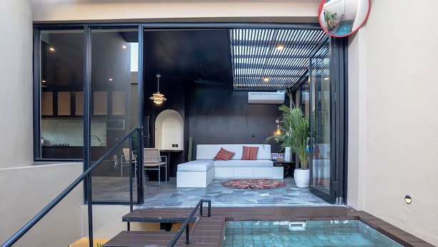 Un espace piscine extérieur moderne doté d’un coin salon fermé par des parois de verre, d’un escalier menant à un deuxième niveau et d’un ventilateur de plafond.