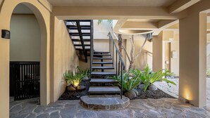 Un hall d’entrée au sol en pierre, avec un escalier, un arbre et des plantes en pot.