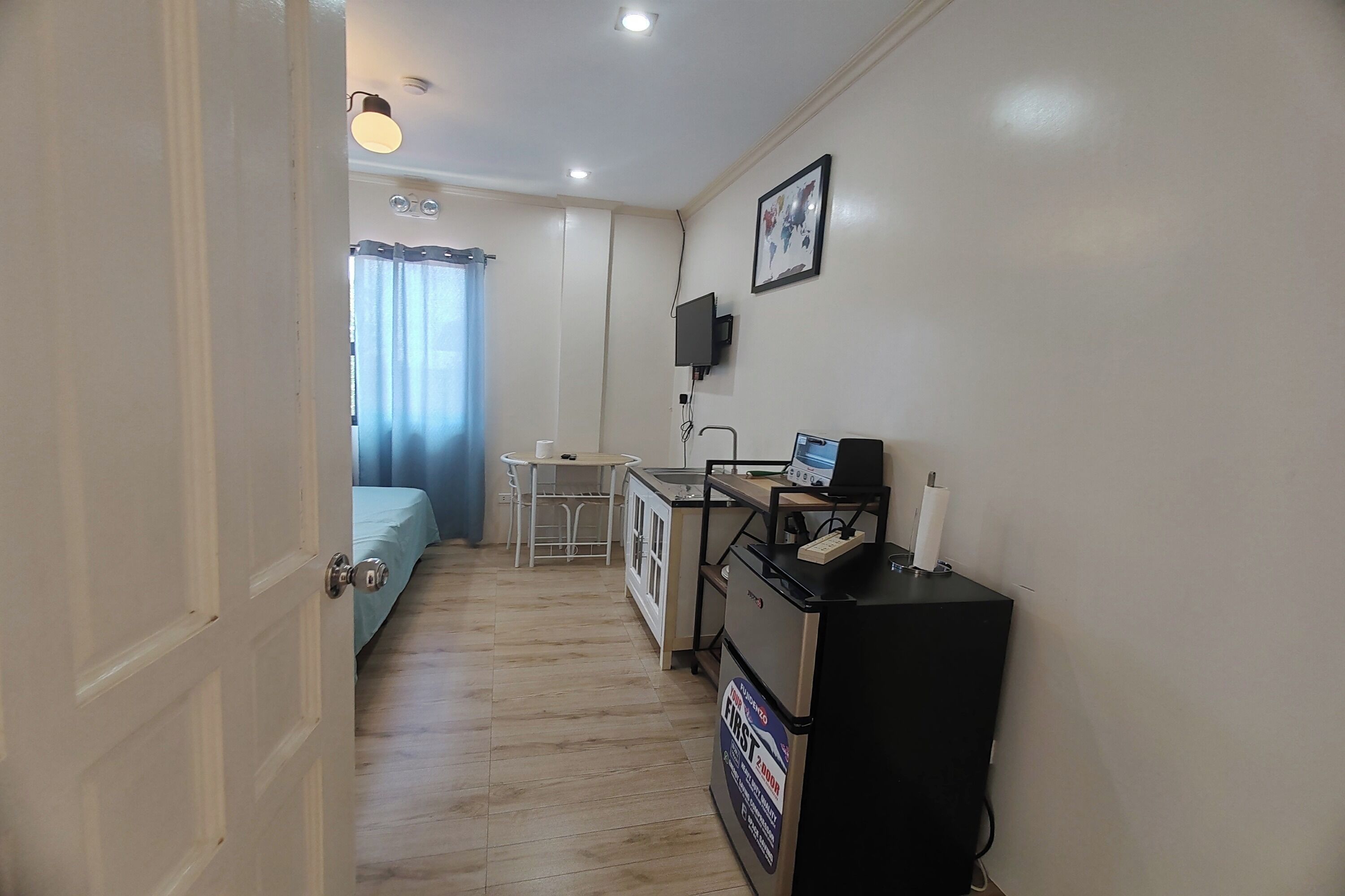 Une petite pièce comprenant un lit, un bureau, une chaise, une petite table et un téléviseur fixé au mur.