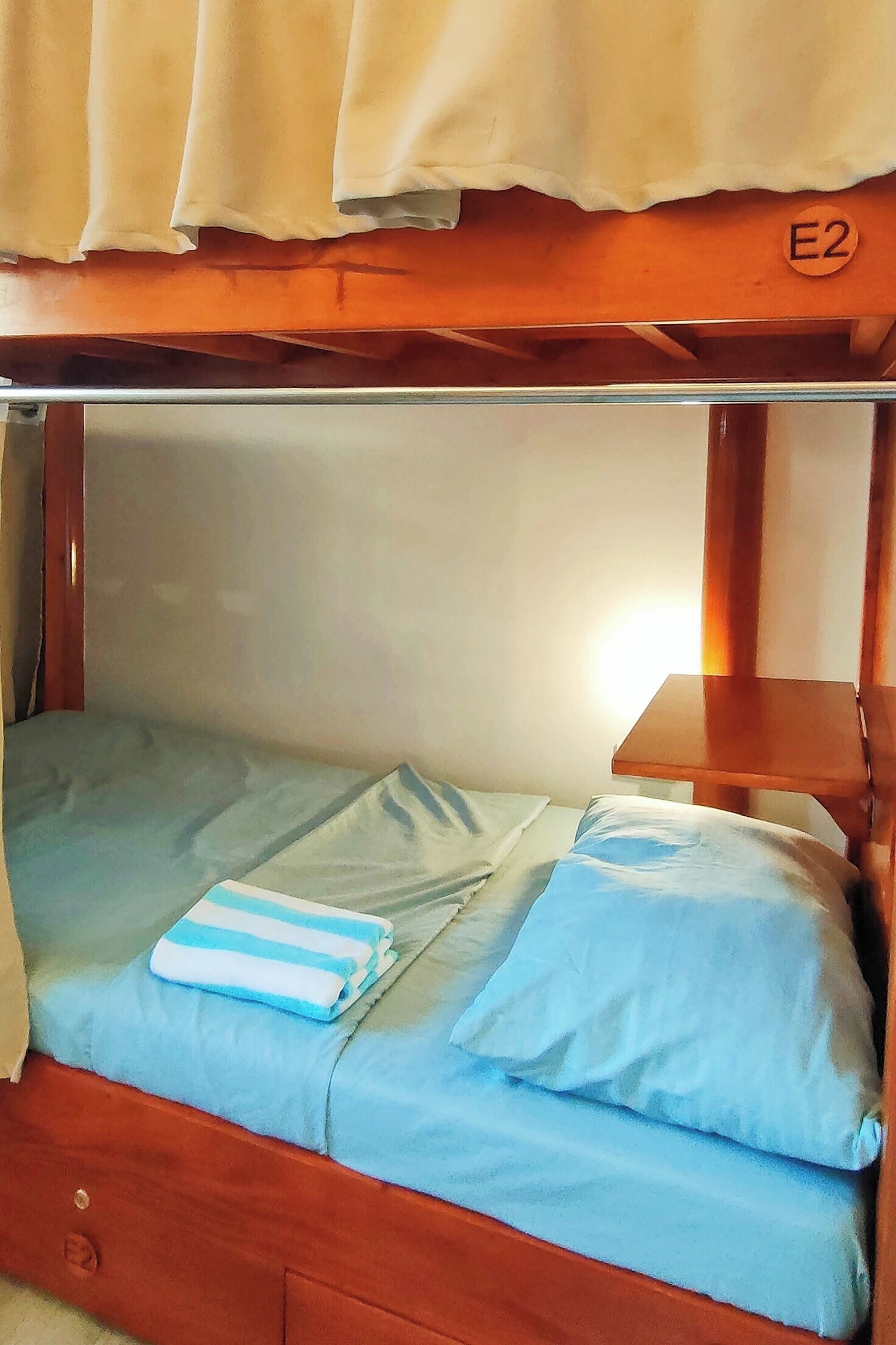 A bunk bed with a blue mattress and pillows, a wooden headboard, and a small table with a lamp.