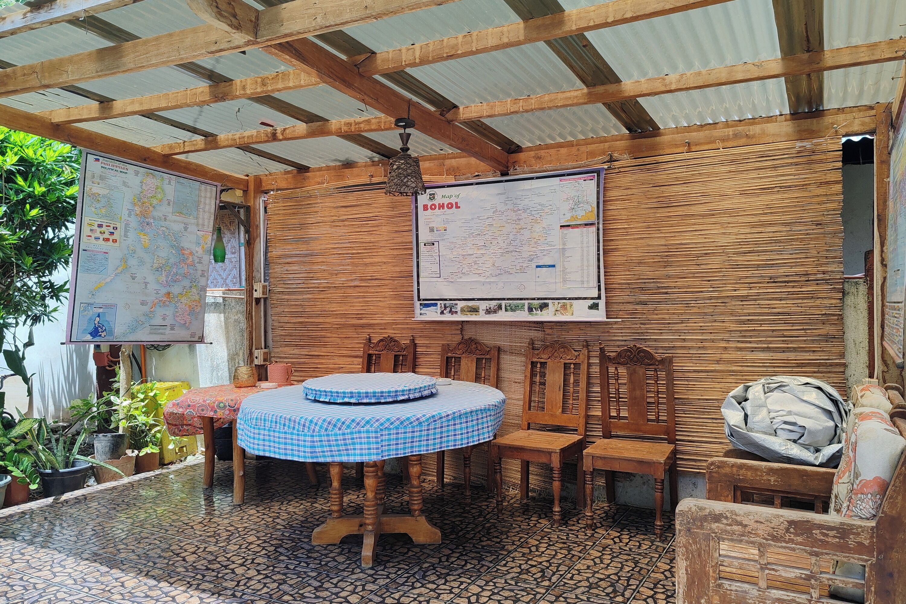 A covered outdoor seating area with a round table, wooden chairs, and a map on the wall.