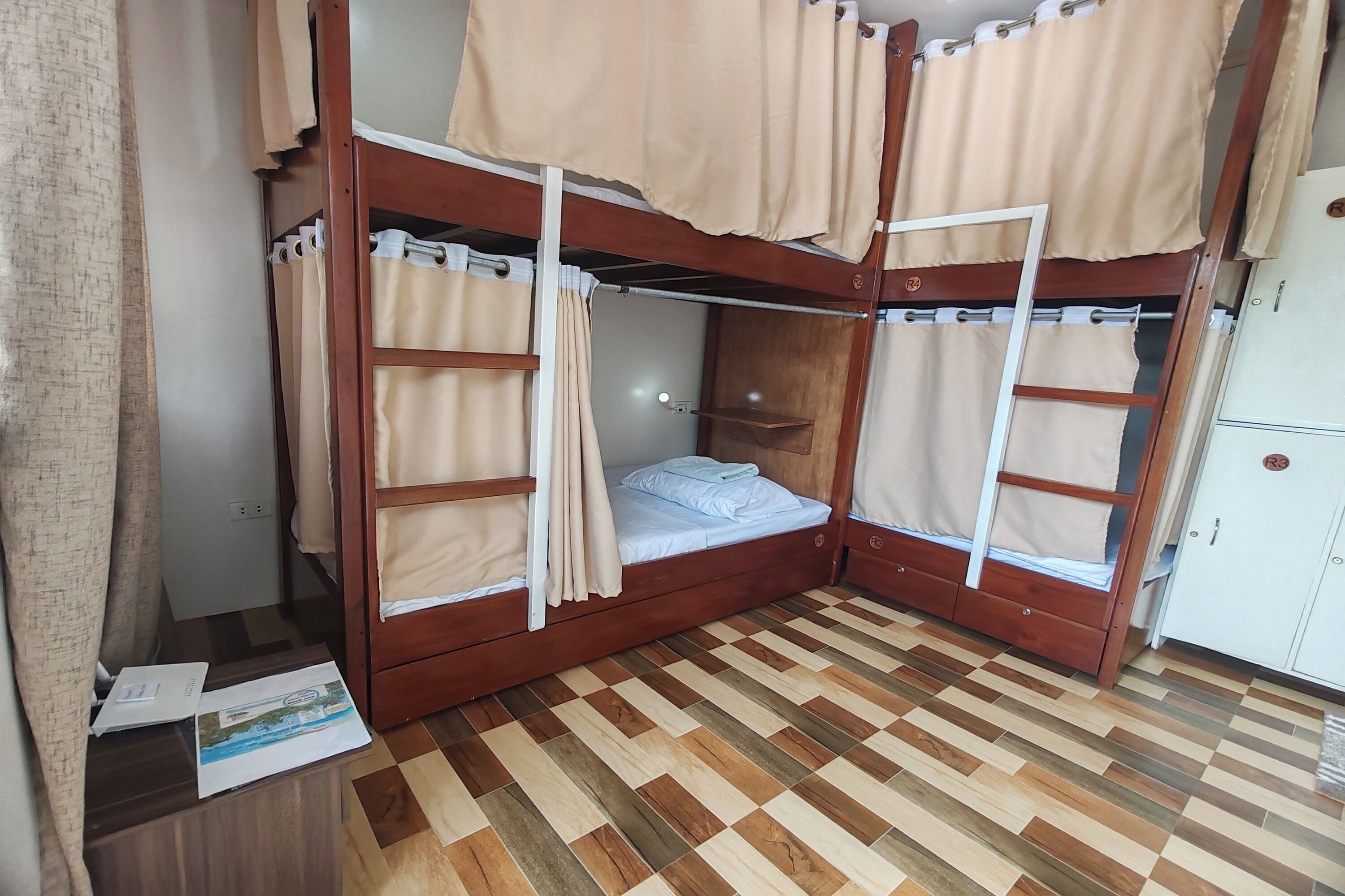 A bunk bed room with curtains, a wooden floor, and a cabinet.