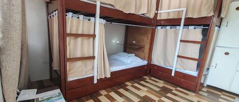 A bunk bed room with curtains, a wooden floor, and a cabinet.