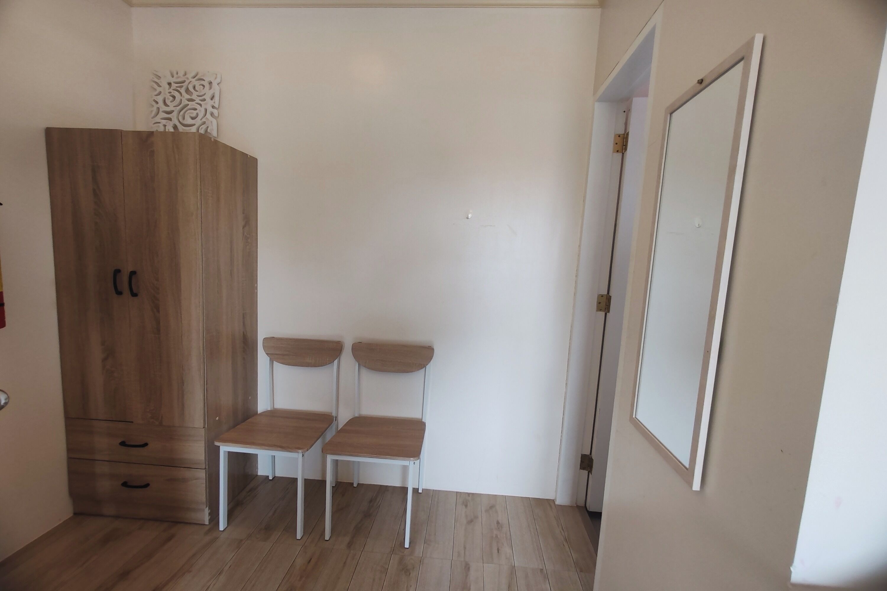 Una habitación con un armario de madera, dos sillas blancas y una puerta blanca.