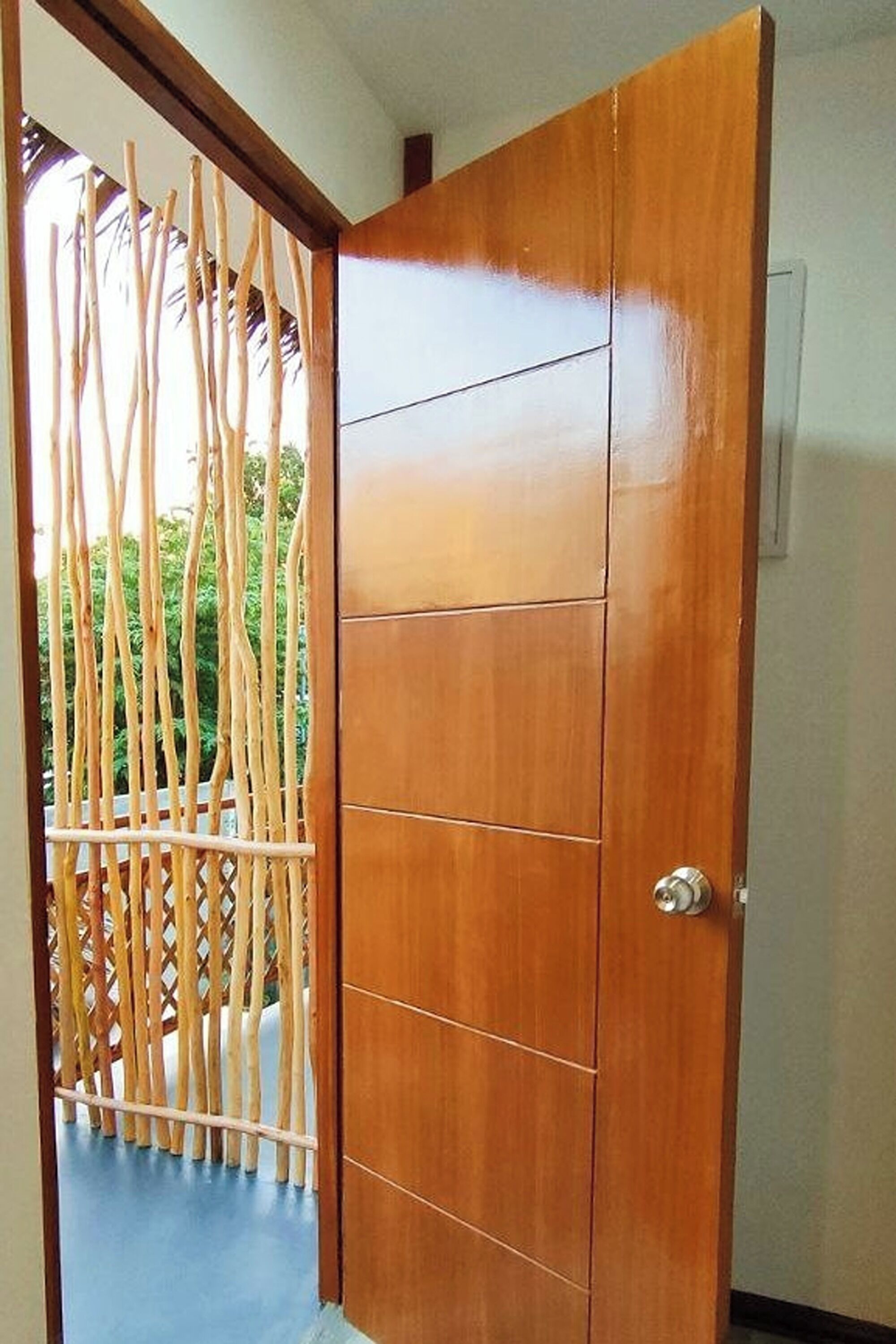 A wooden door with a metal handle, a blue floor, and a bamboo fence in the background.