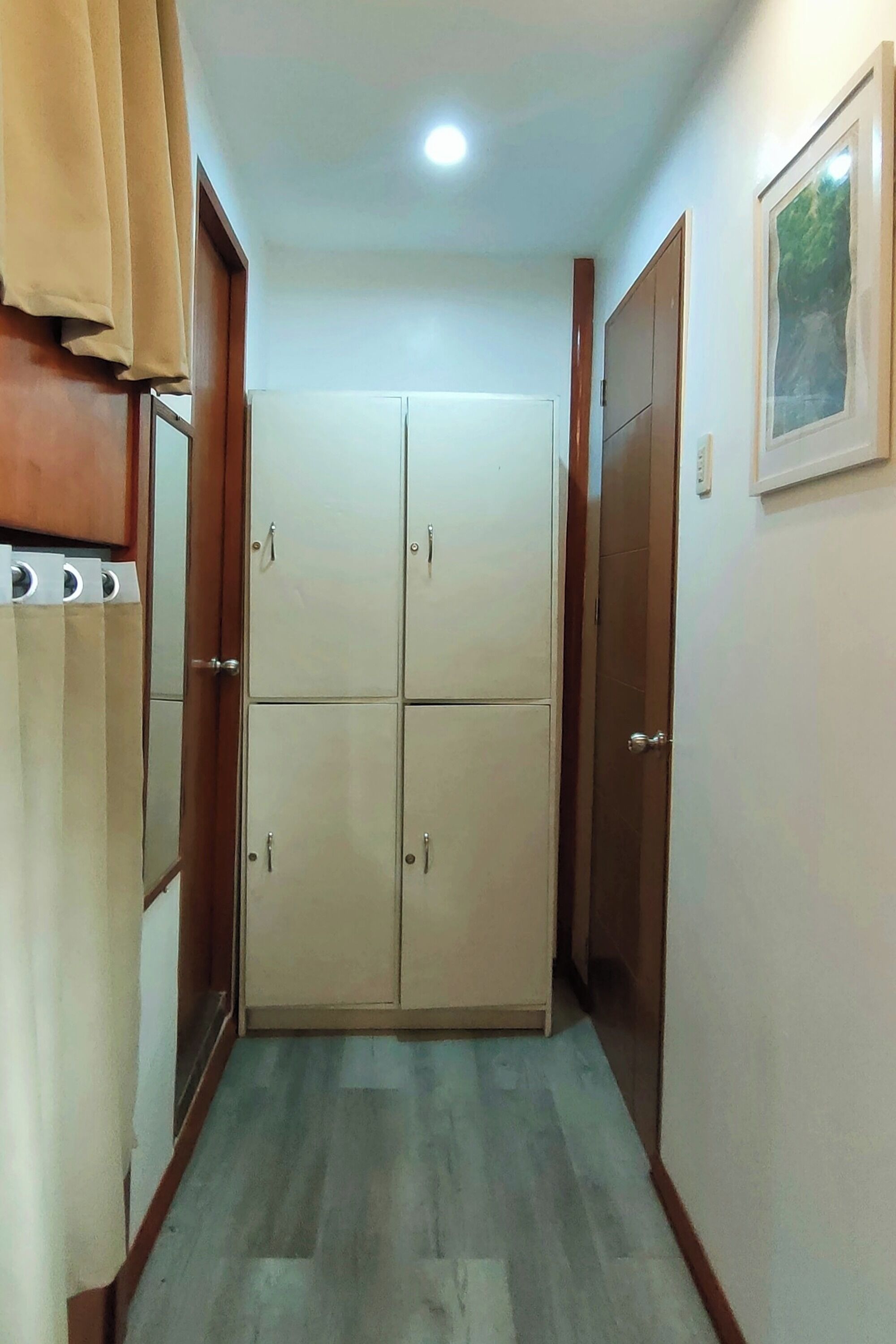 A narrow hallway with a wooden wardrobe on the left, a beige wardrobe in the center, and a wooden door on the right.