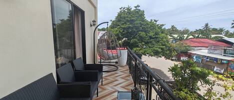 A balcony with a patterned floor, black wicker furniture, and a glass table.