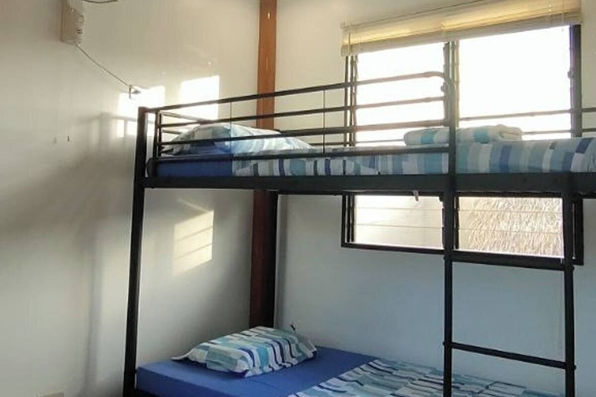 A dormitory room with bunk beds, a ceiling fan, and a window providing natural light.