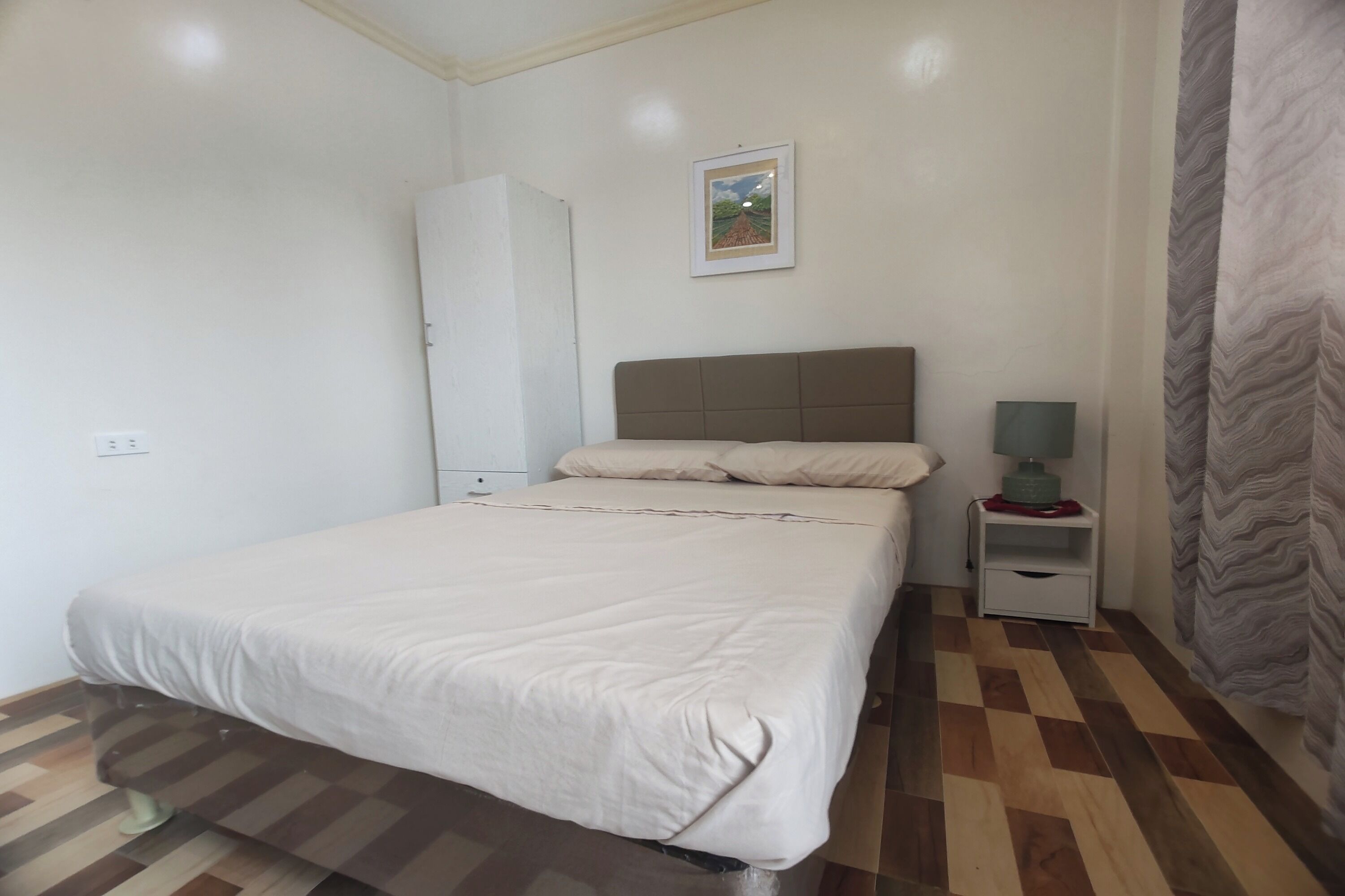 Un dormitorio con cama, mesita de noche, lámpara, armario y un cuadro en la pared.
