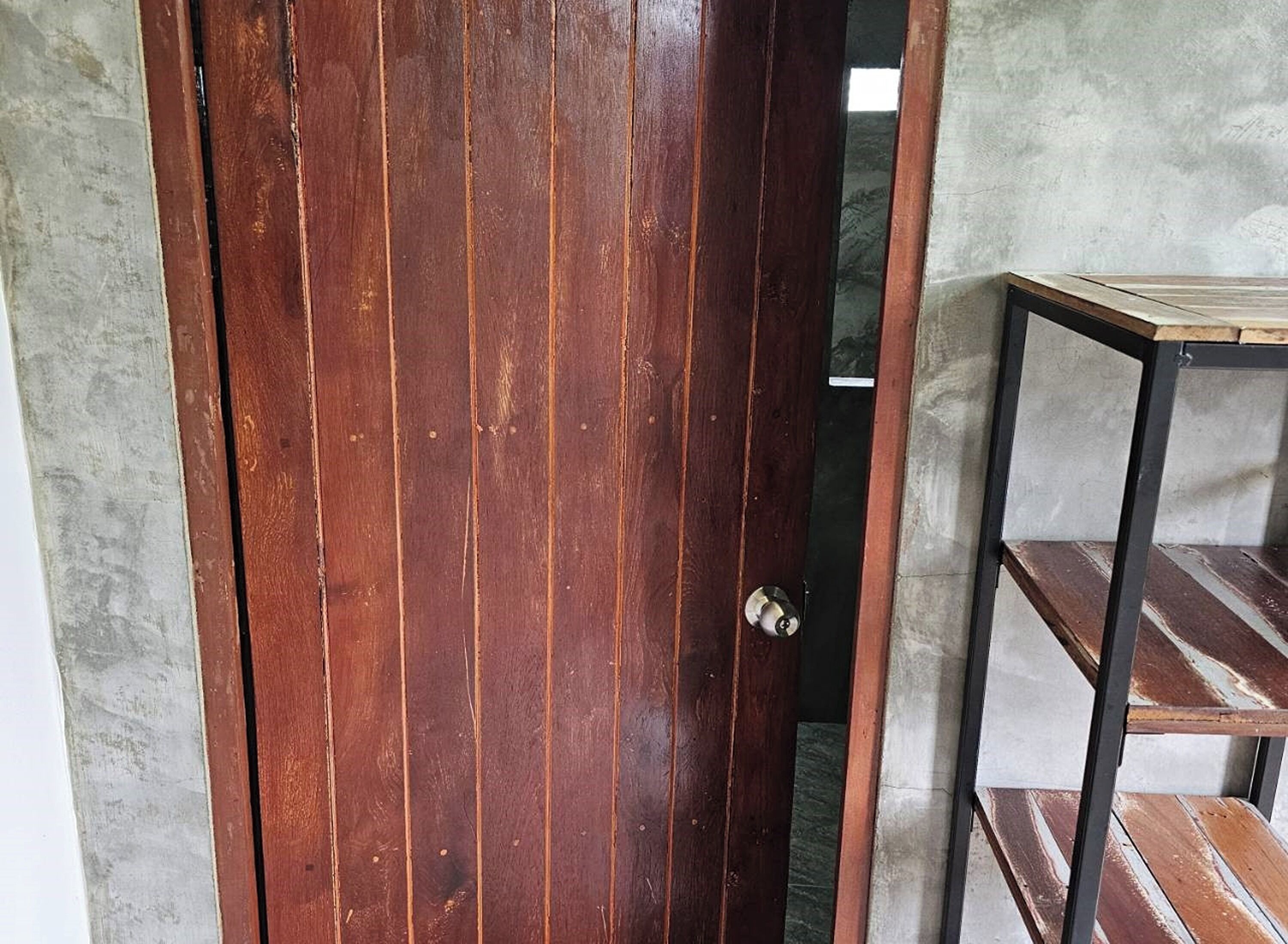 A wooden door with a metal handle, a metal shelf unit with a wooden top, and a concrete wall.