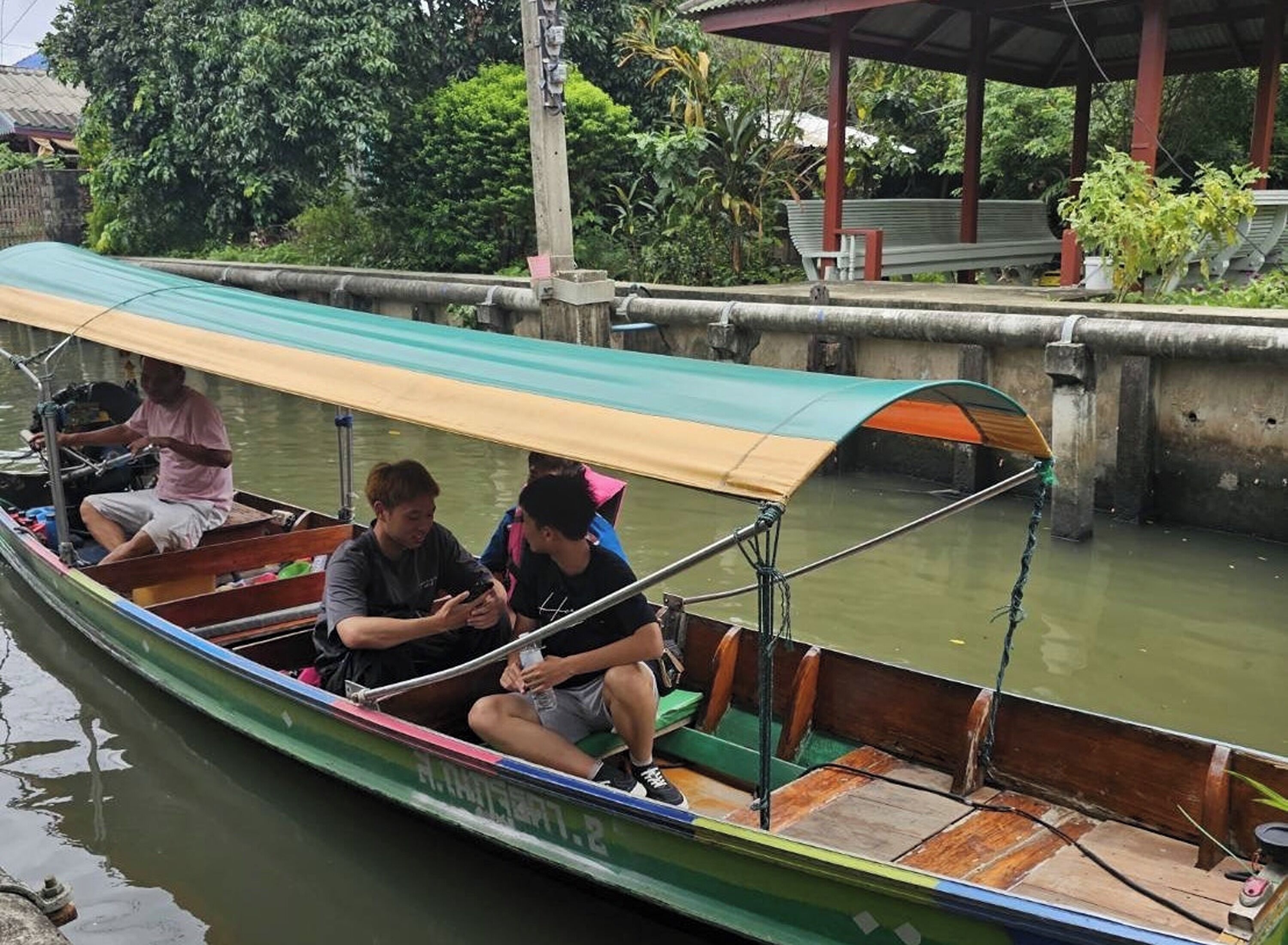 Un bote estrecho con toldo, pasajeros y amarrado.