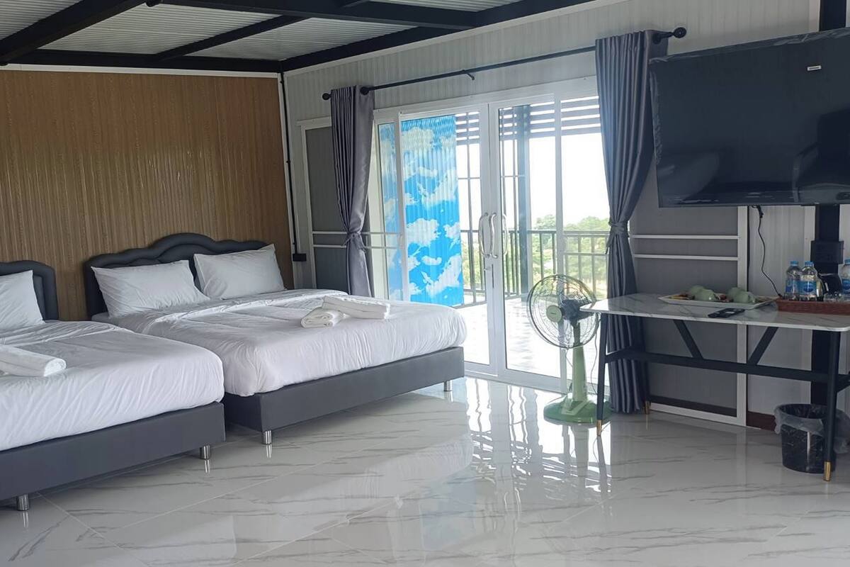 A hotel room with two beds, a TV, a fan, and a balcony with a view.