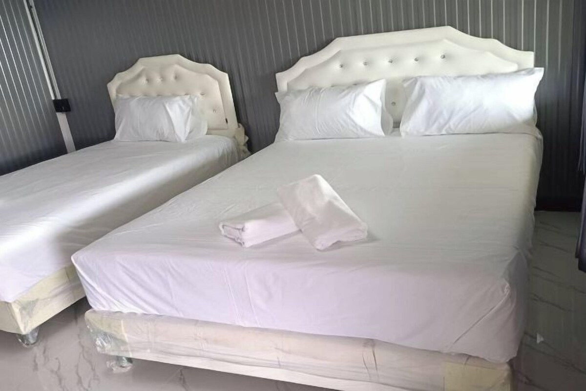 Two beds with white headboards and bedding, a folded towel on the larger bed, and a metallic wall.